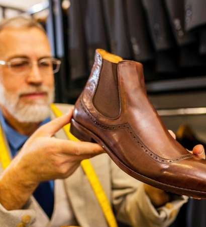 elder good looking man with gray beard wear nice suit at atelier studio and checking the quality of handmade itatian shoe.