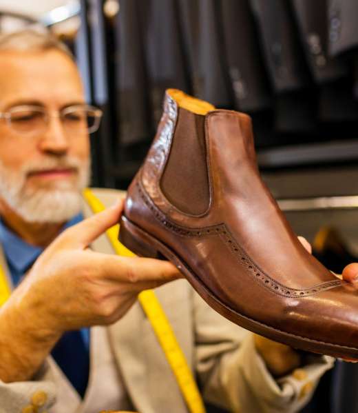 elder good looking man with gray beard wear nice suit at atelier studio and checking the quality of handmade itatian shoe.